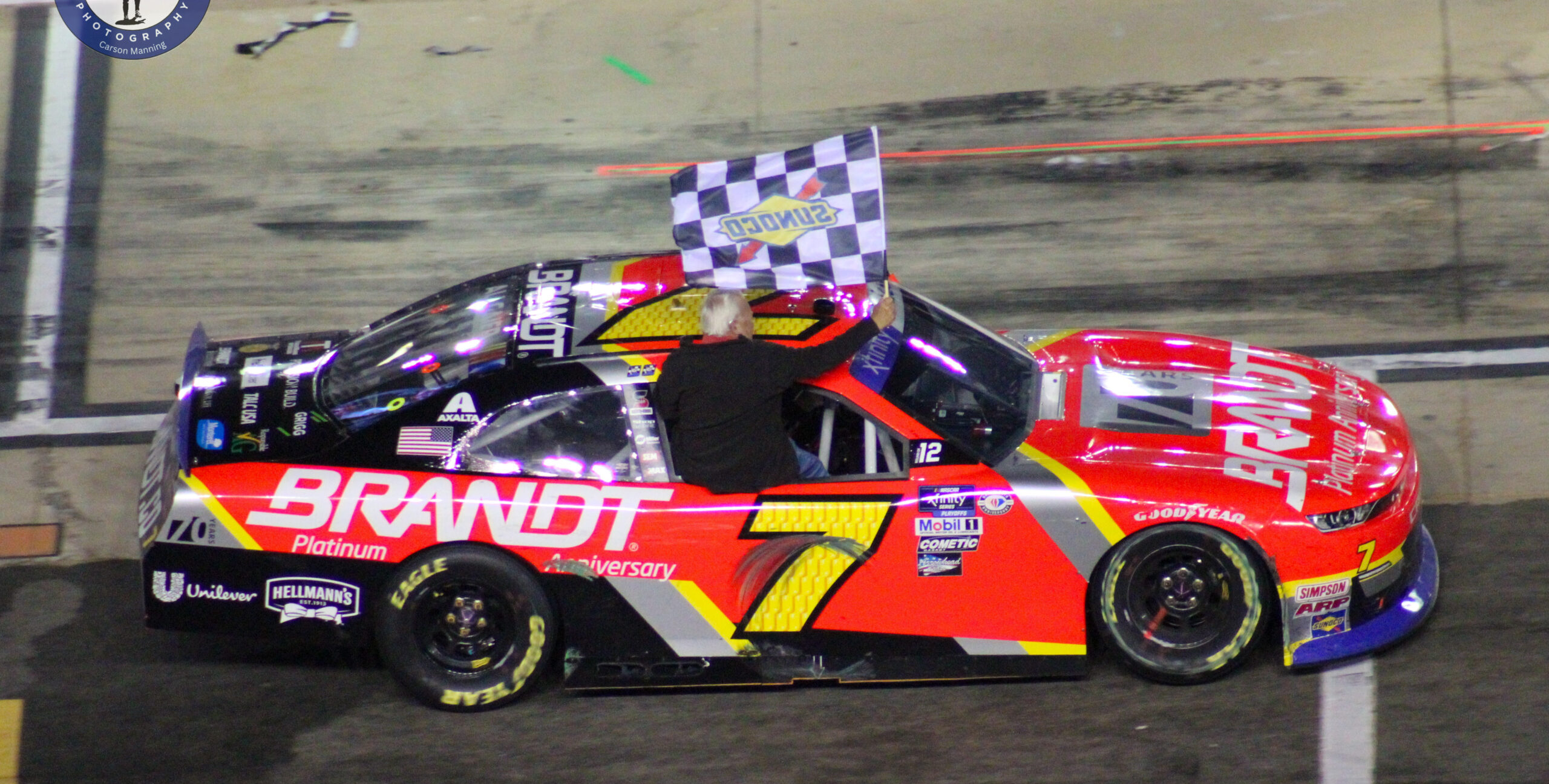 Justin Allgaier holding the checkered flag out his window on his way to victory lane after the Xfinity Bristol Night Race